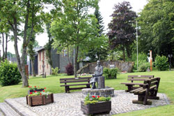 Dorfgarten mit Löffelschnitzerskulptur und dem Ehrenmal neben der Martin-Luther-Kirche in Langewiese